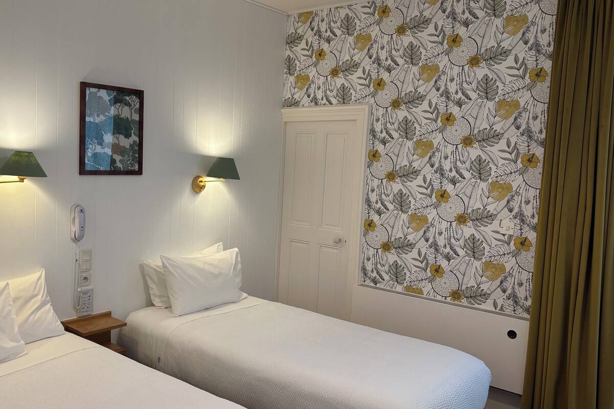 A room with two beds, a wall-mounted telephone, and a painting.
