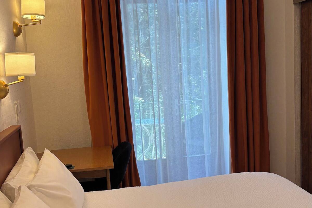 A hotel room with a bed, a desk, a lamp, and a window with curtains.
