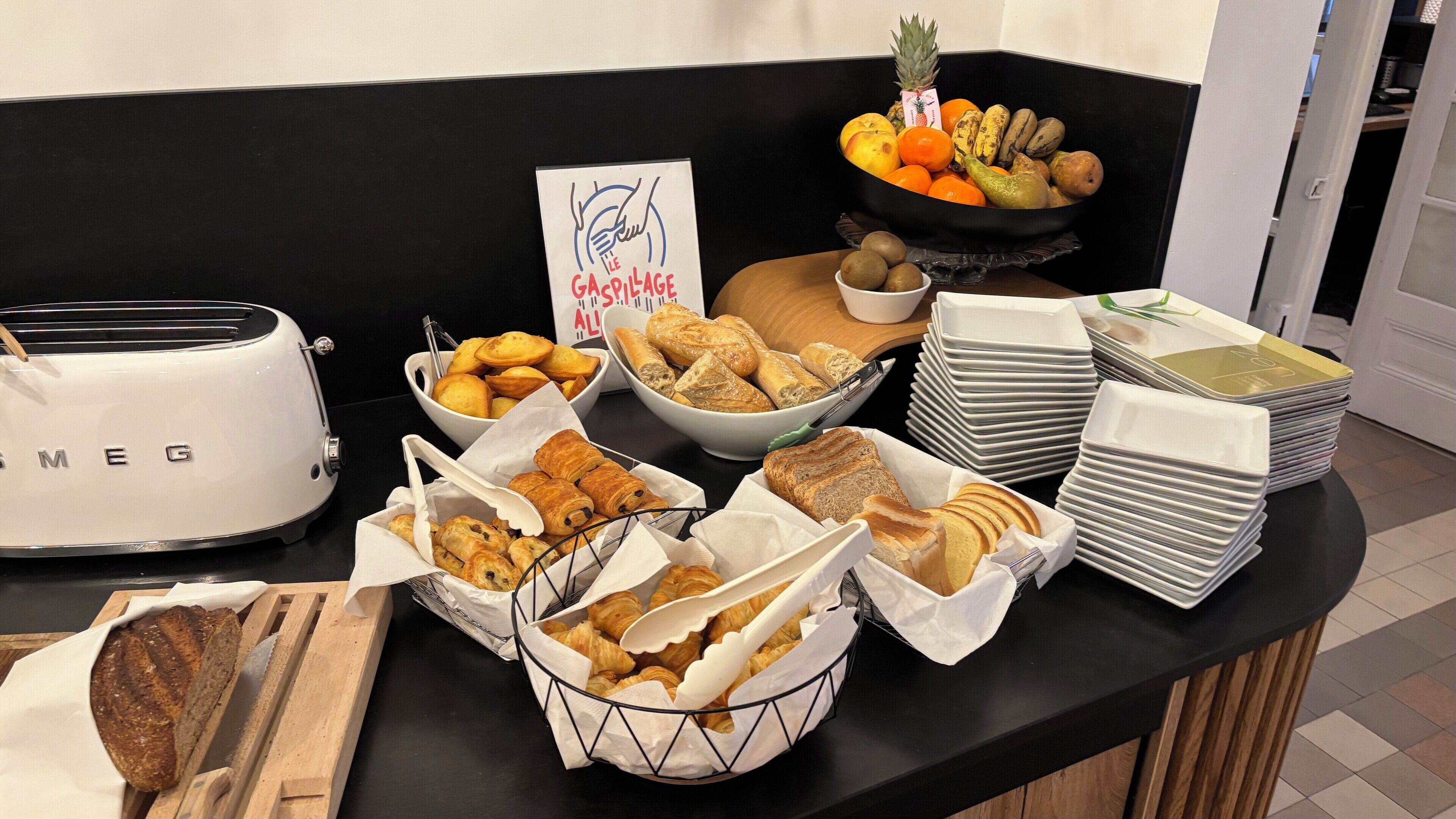 Une table de buffet proposant divers aliments, notamment du pain, des pâtisseries et des fruits.