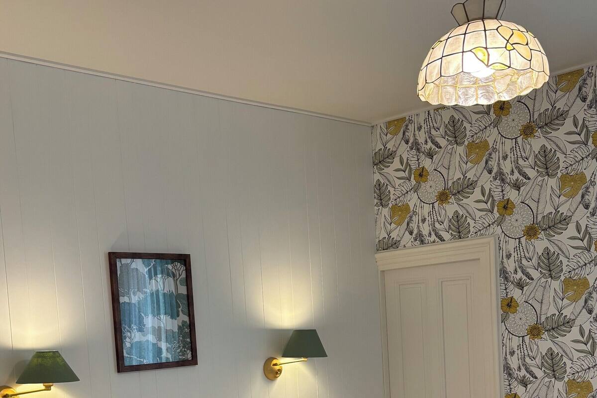 A hotel room with two beds, a wall-mounted telephone, a framed picture, and a floral wallpaper pattern.