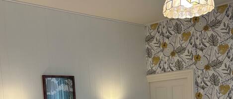 A hotel room with two beds, a wall-mounted telephone, a framed picture, and a floral wallpaper pattern.