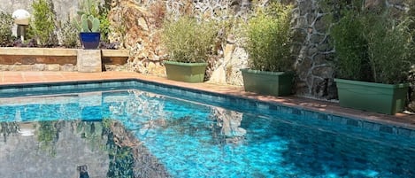 Una piscina con agua cristalina azul, rodeada de muros de piedra y plantas en macetas.