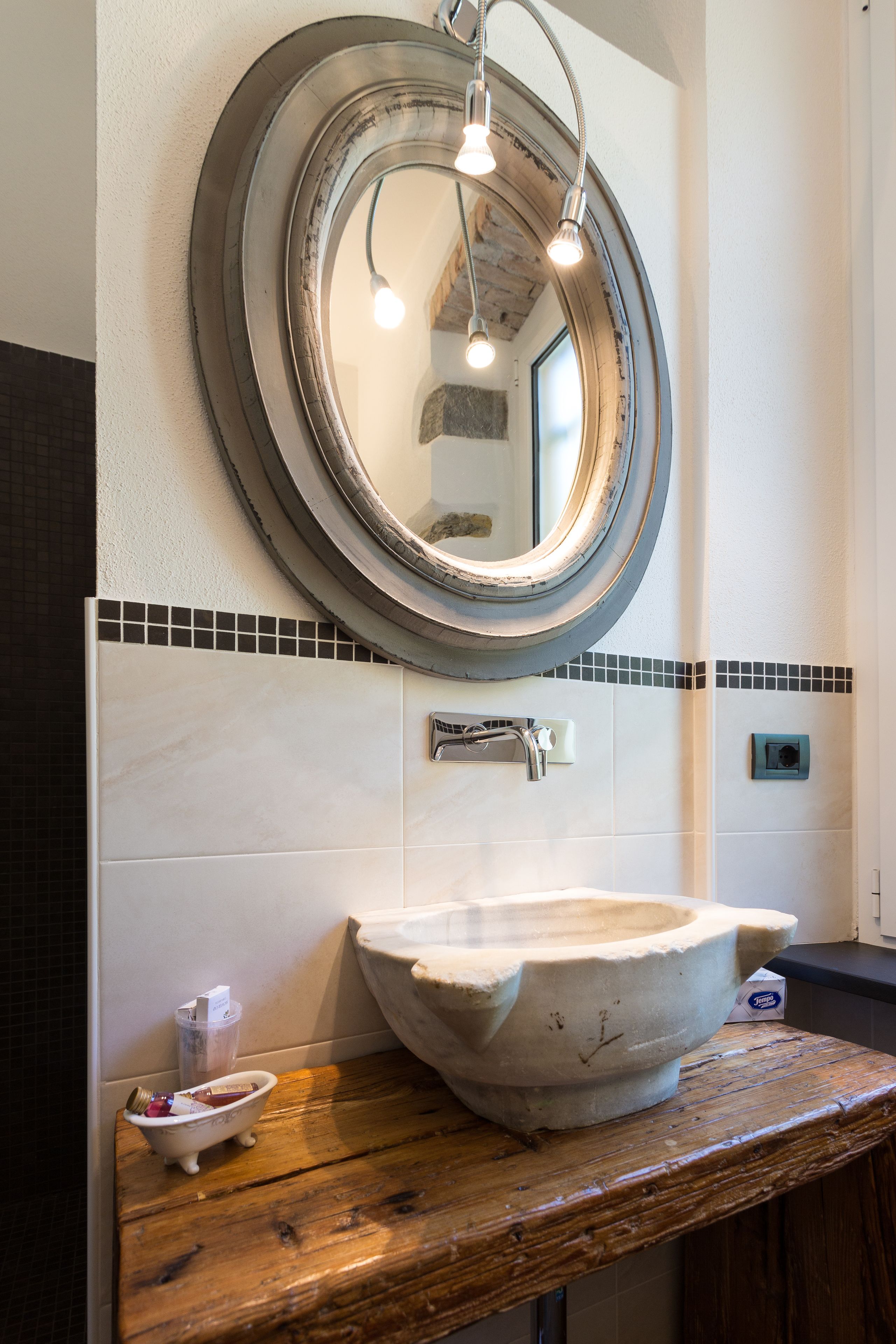 A bathroom with a large oval mirror, a stone sink, and a wooden countertop.