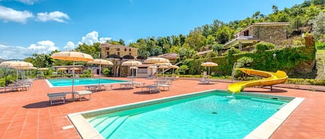 A swimming pool with a yellow slide, lounge chairs, and umbrellas.