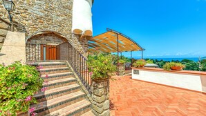 A stone building with a staircase leading to a wooden door, a covered outdoor area with a herringbone-patterned floor, and a view of the sea. - Hotel Hermitage (Castellabate)