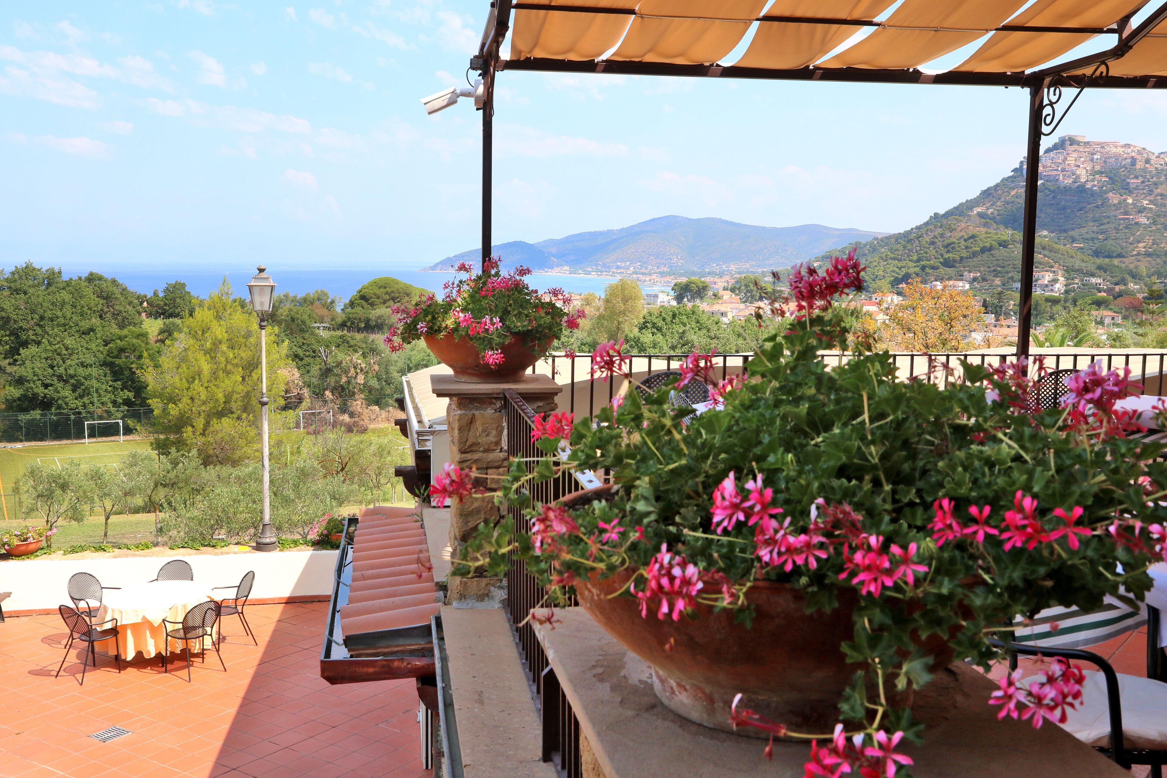 Eine Terrasse mit Tisch und Stühlen, ein großer Pflanzkübel mit Blumen und Blick auf das Meer und die Hügel.