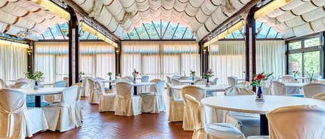 A banquet hall with round tables, white chairs, and a high ceiling with a patterned design.