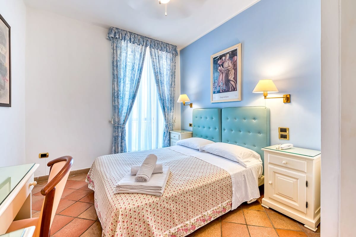A bedroom with a bed, two bedside lamps, a nightstand, a chair, and a painting on the wall.