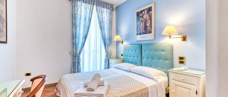 Un dormitorio con una cama, dos lámparas de noche, una mesita de noche, una silla y un cuadro en la pared.