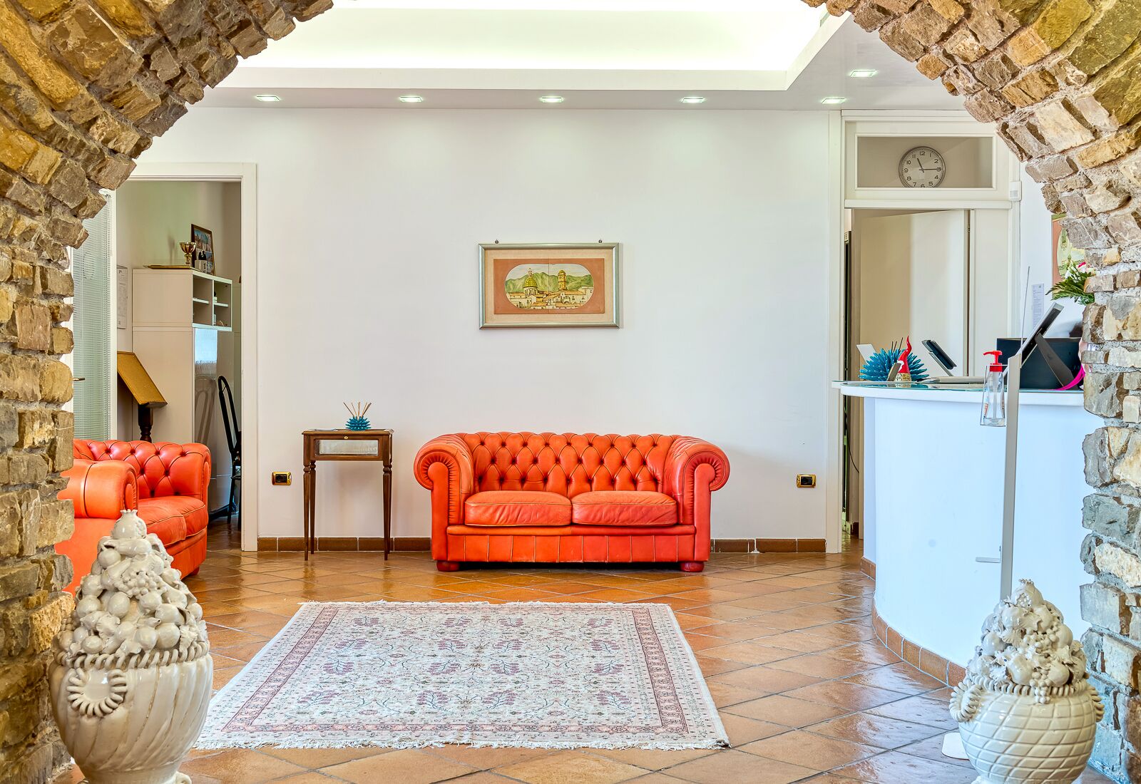 Ein Wohnzimmer mit einem roten Sofa, einem gemusterten Teppich und einem gerahmten Bild an der Wand.