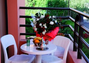 A balcony with a table set for two, a bouquet of flowers, and a fruit bowl. - Résidence Appart hotel Assounfou (Marrakech)