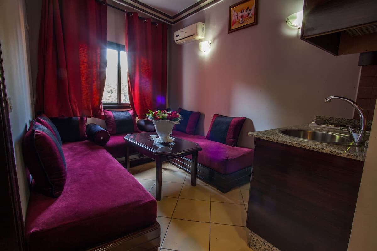 A compact living space with a sofa, a small table, a kitchen area with a sink, and an air conditioning unit.
