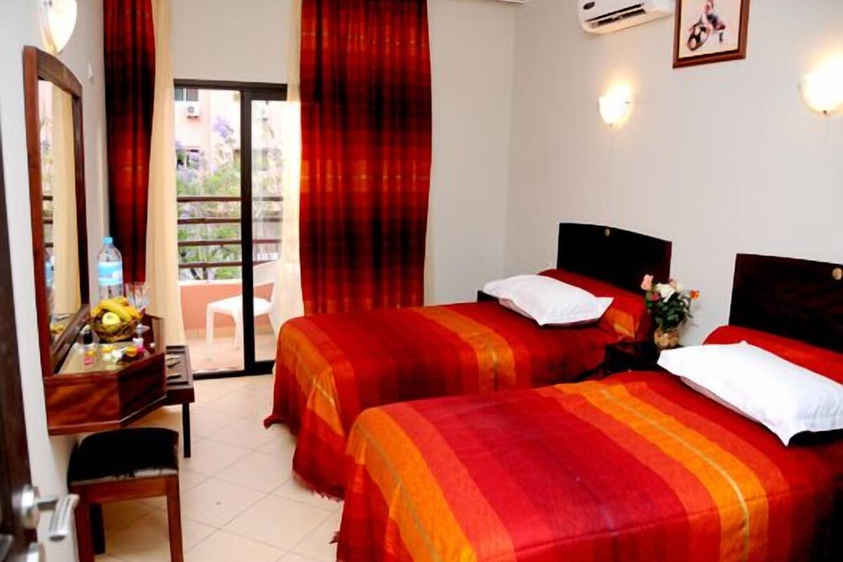 A hotel room with two beds, a desk with a mirror, and a view of the outside through a glass door.