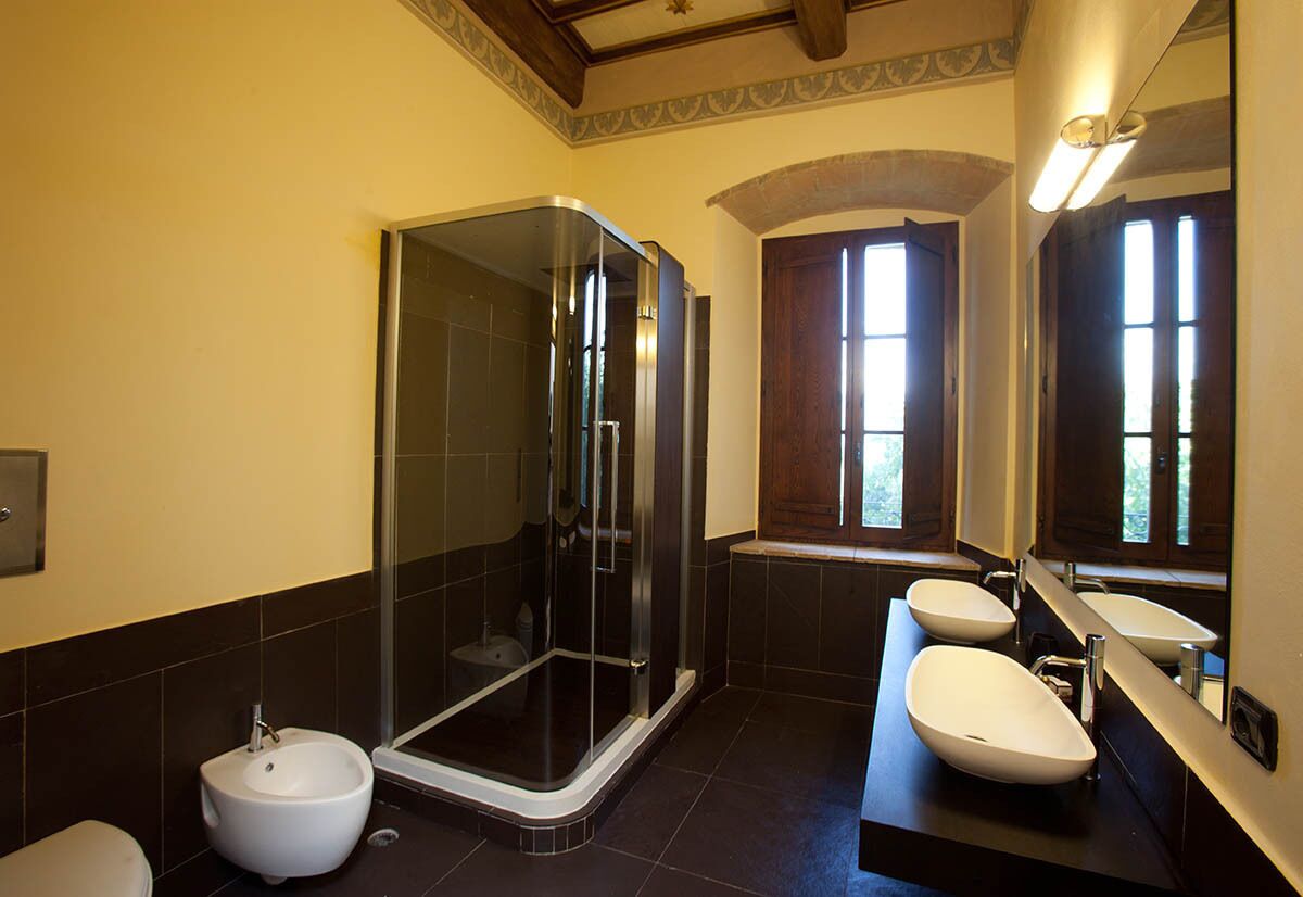 A modern bathroom with a glass-enclosed shower, a bidet, and two sinks with mirrors.