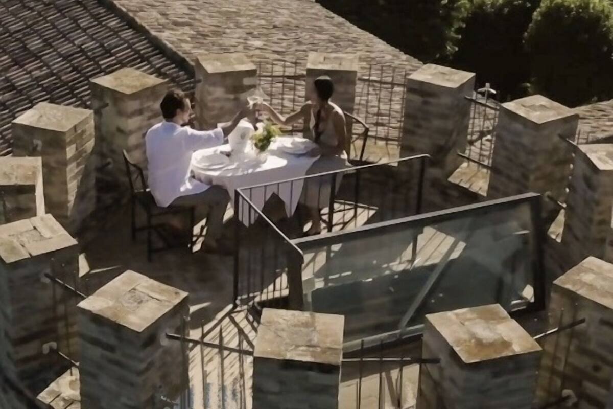 A circular outdoor dining area with a stone table and chairs, surrounded by stone walls and a glass railing.