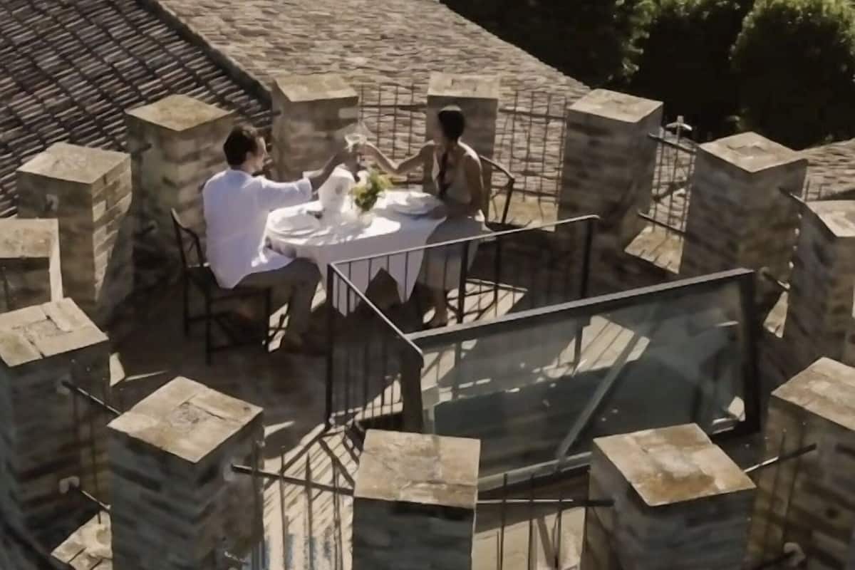 A circular outdoor dining area with a stone table and chairs, surrounded by stone walls and a glass railing.