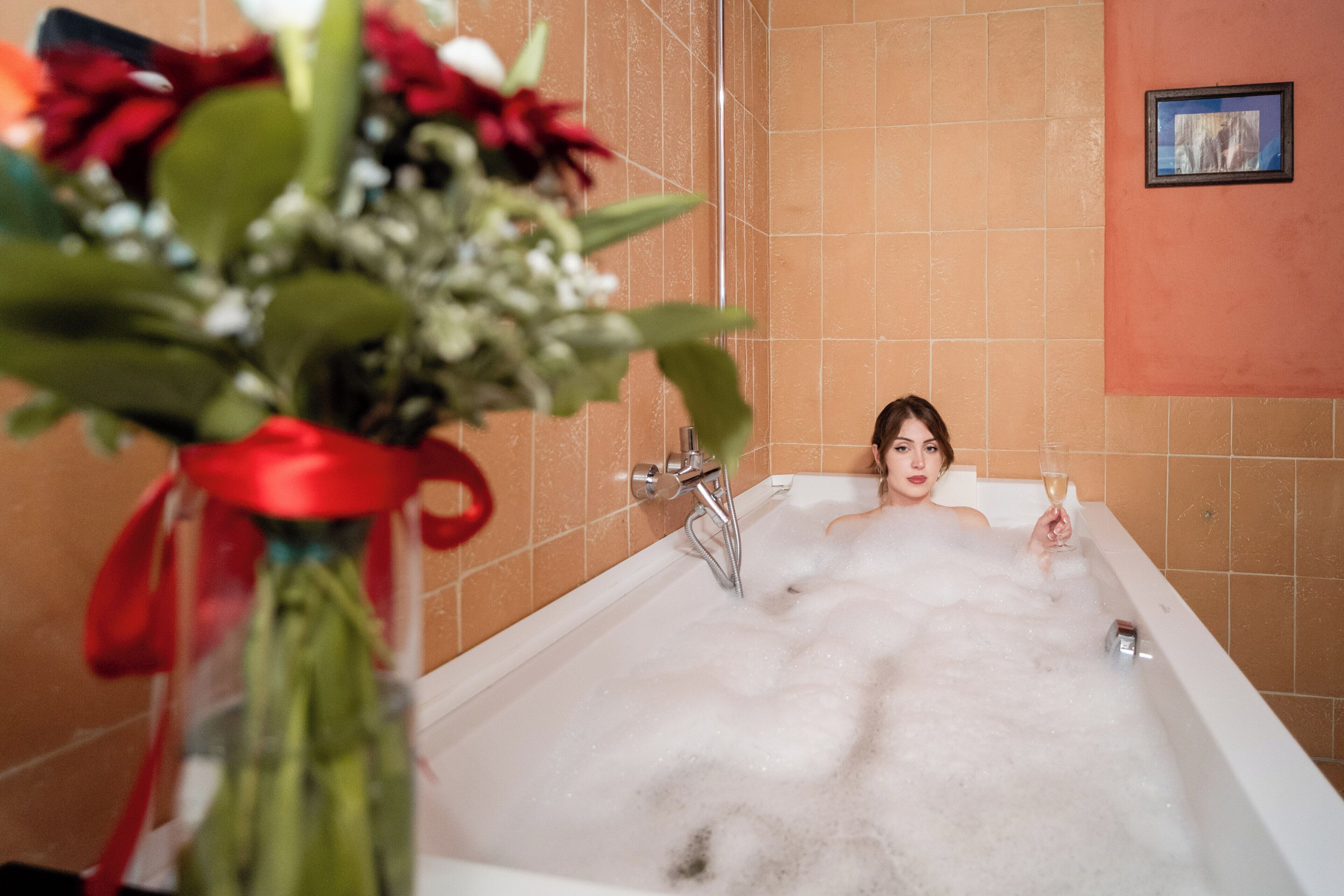 A bathtub filled with bubbles, a bouquet of flowers, and a glass of champagne.