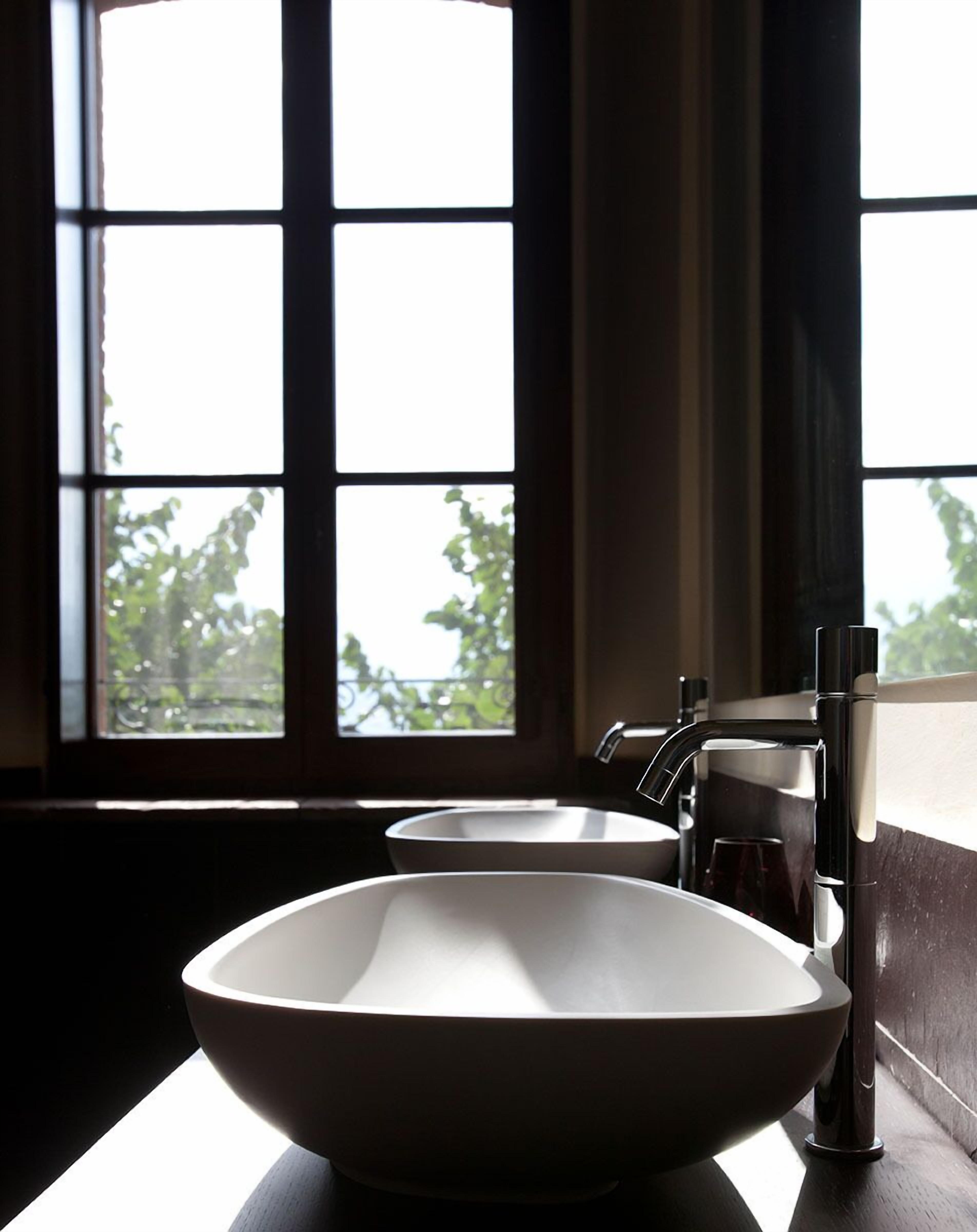 A bathroom with a large window, a white sink, and a modern faucet.