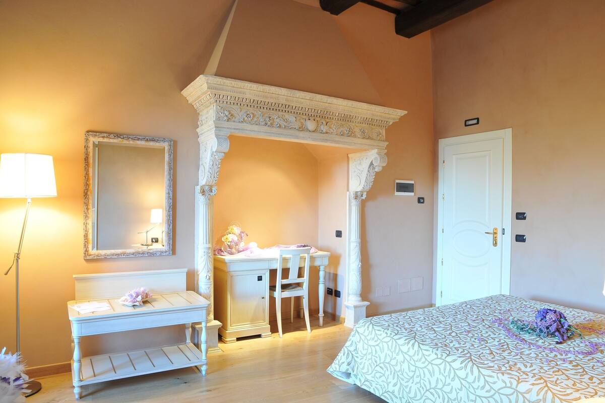 A bedroom with a bed, a desk, a chair, a mirror, and a lamp.