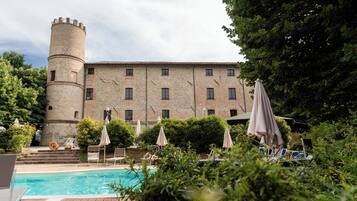 Ein schlossartiges Gebäude mit Schwimmbad, umgeben von Grünflächen und Außenmöbeln.