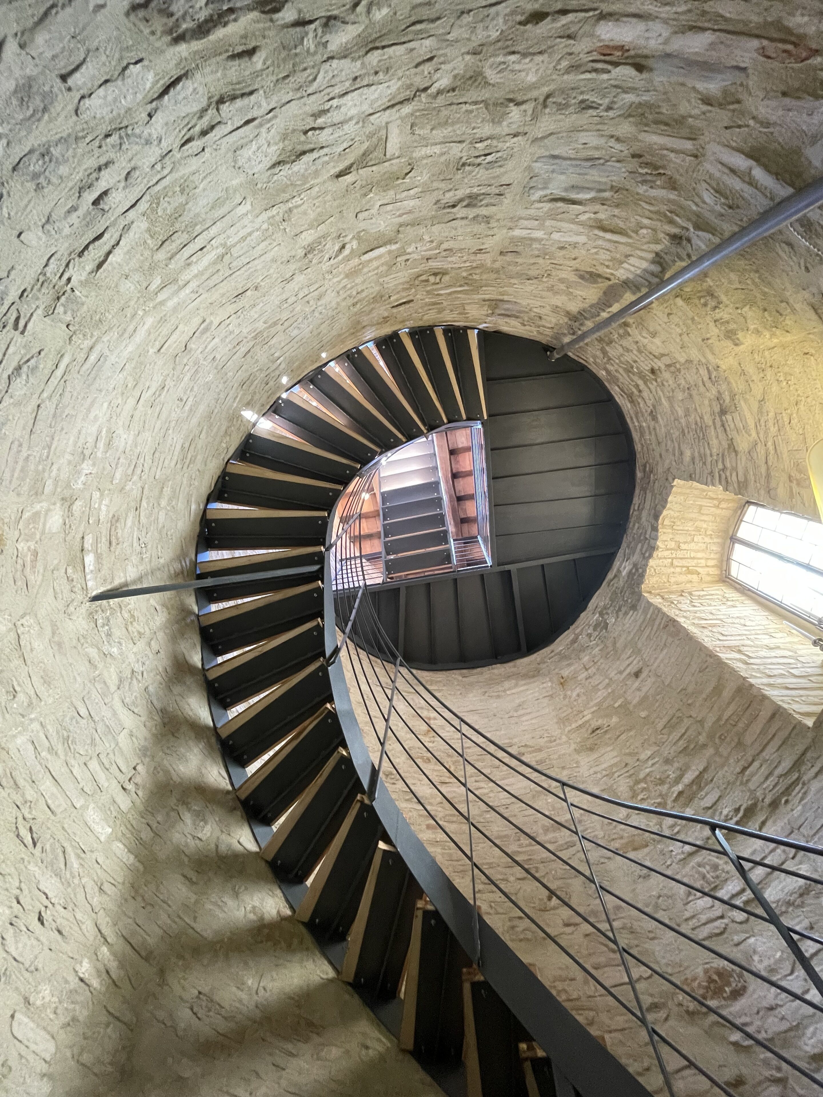A spiral staircase with a wooden handrail and metal balusters, set in a stone-walled interior.