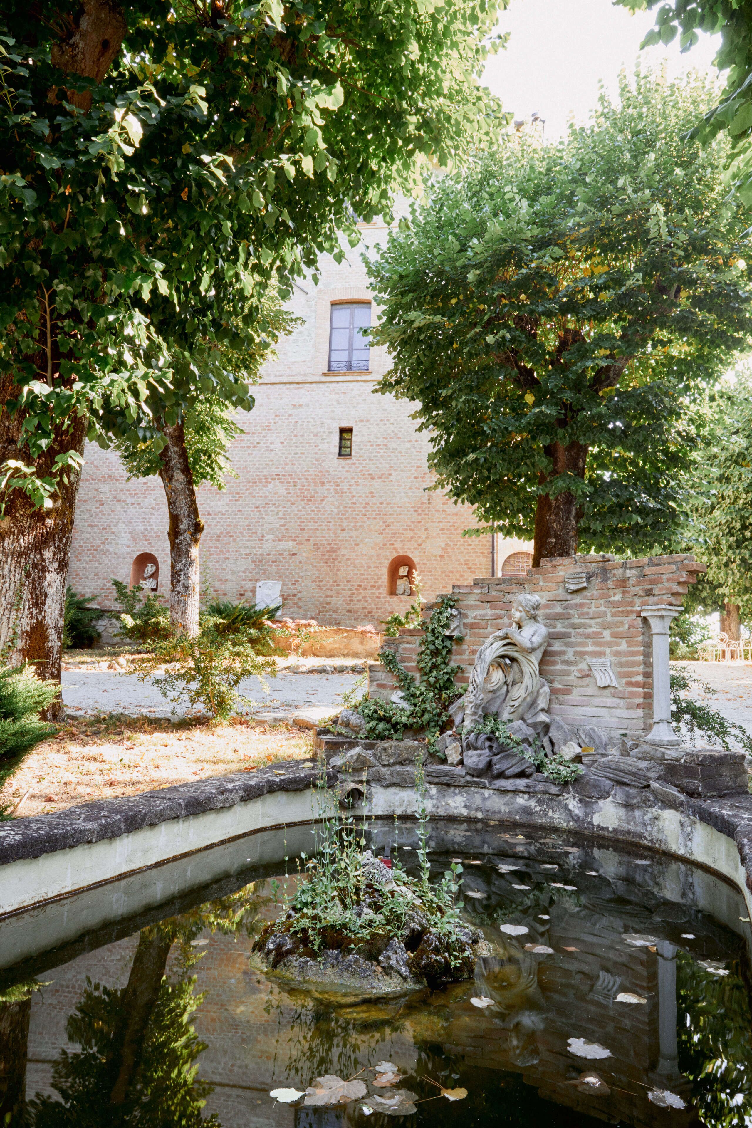 Un patio con una fuente, un edificio de ladrillo y árboles.