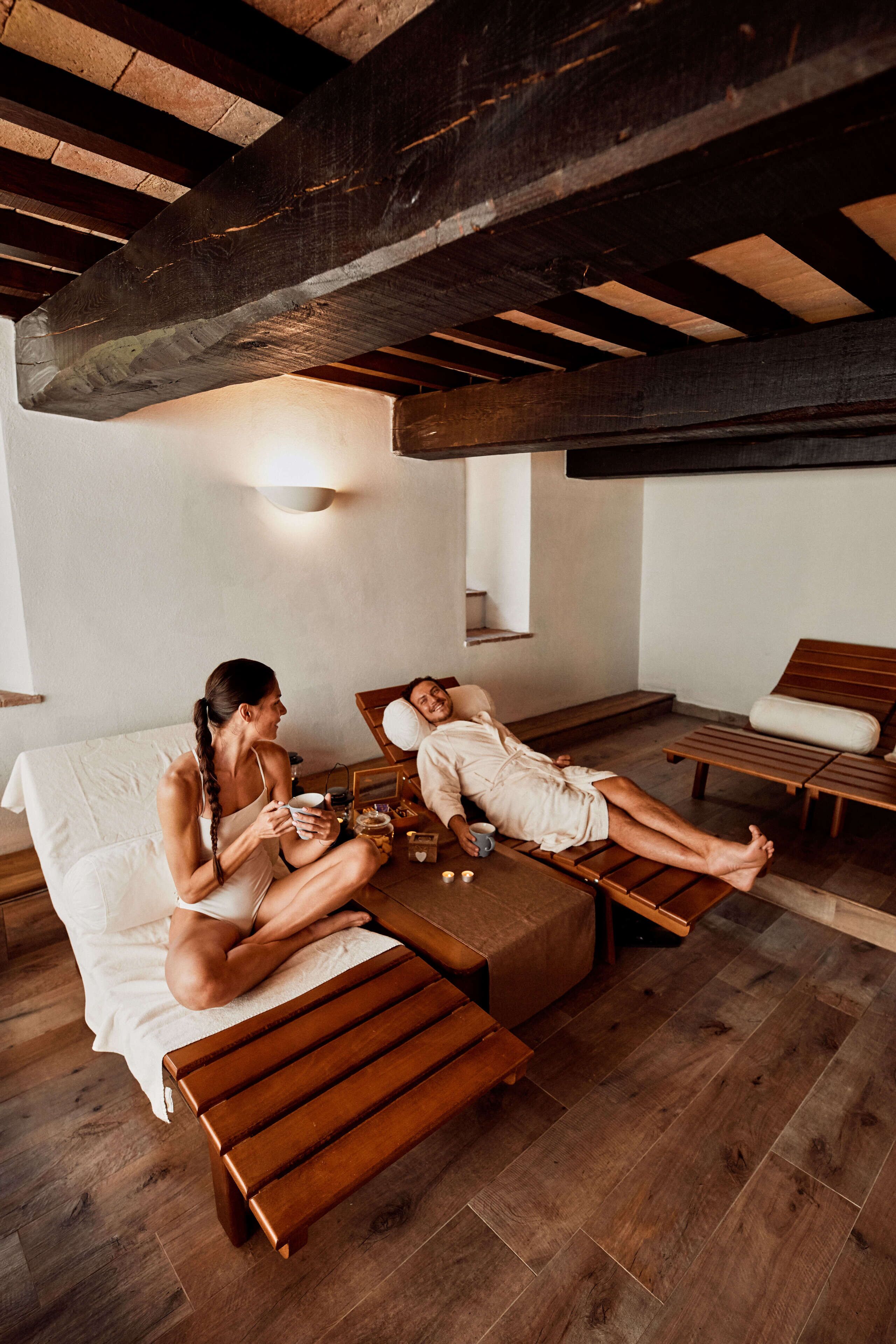 A spa room with wooden floors, a bed, a massage table, and a small table with a cup and a book.