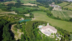 Vista aérea de una extensa propiedad con un edificio central rodeado de exuberante vegetación, una piscina y amplios campos.