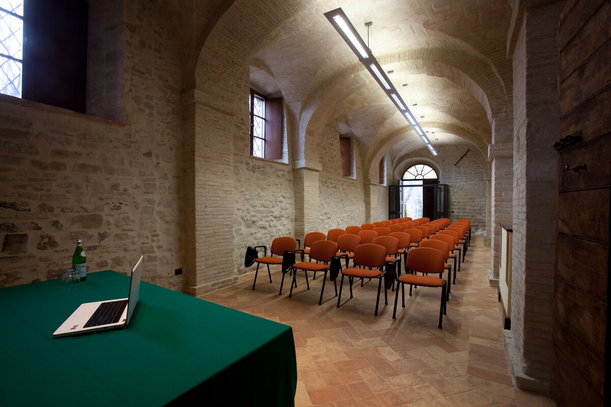 A conference room with a green table, a laptop, and orange chairs arranged in rows.