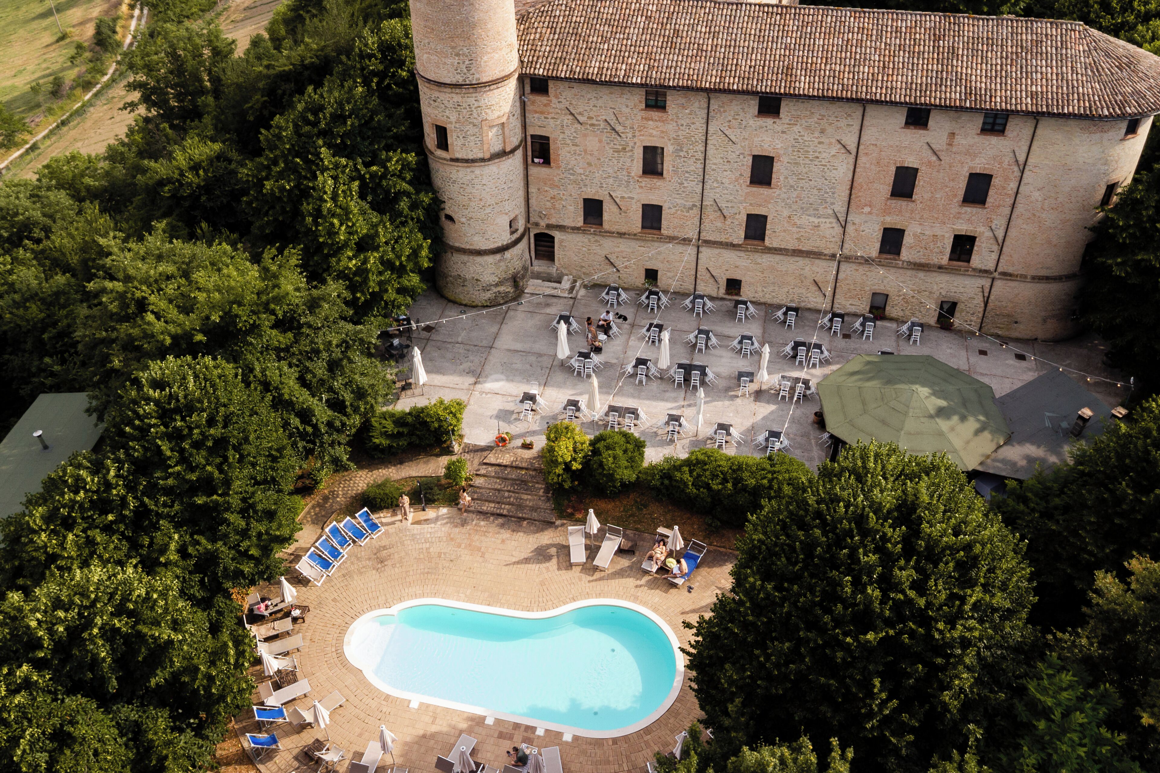 An aerial view of a hotel with a swimming pool, lounge chairs, and a courtyard.