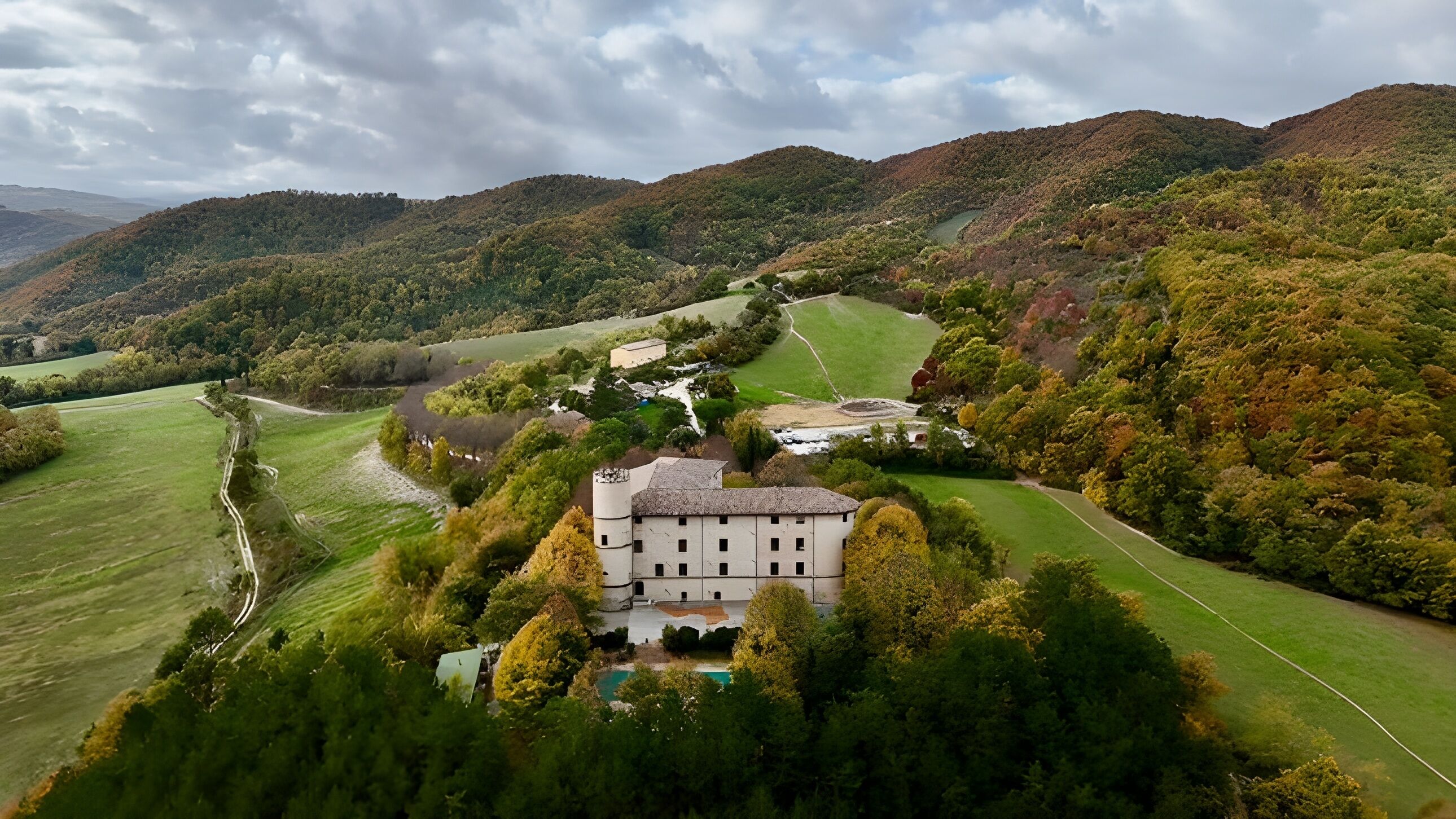 A large, white building surrounded by lush greenery and a winding road.