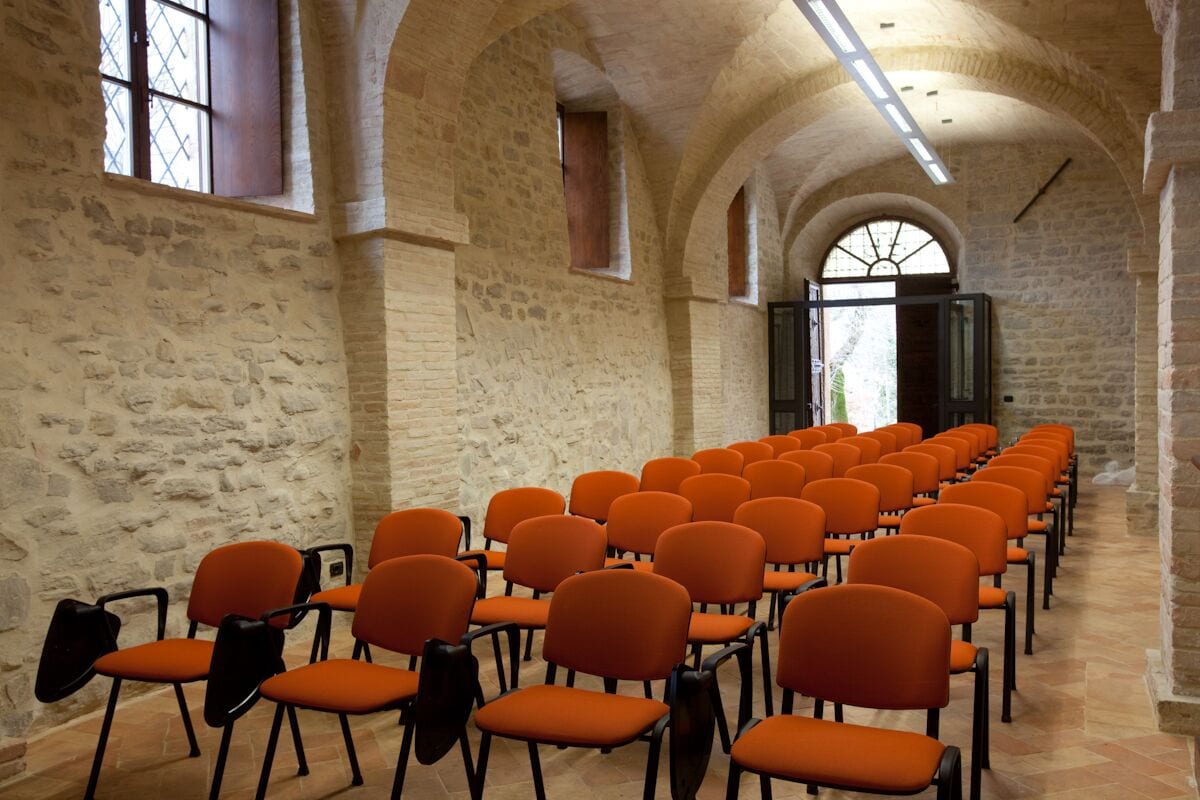 A room with rows of orange chairs, stone walls, and arched ceilings.