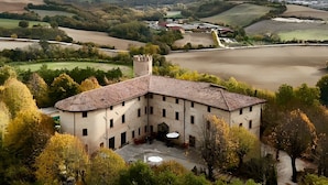 Un edificio grande e histórico con un patio interior, rodeado de abundante vegetación y colinas al fondo.