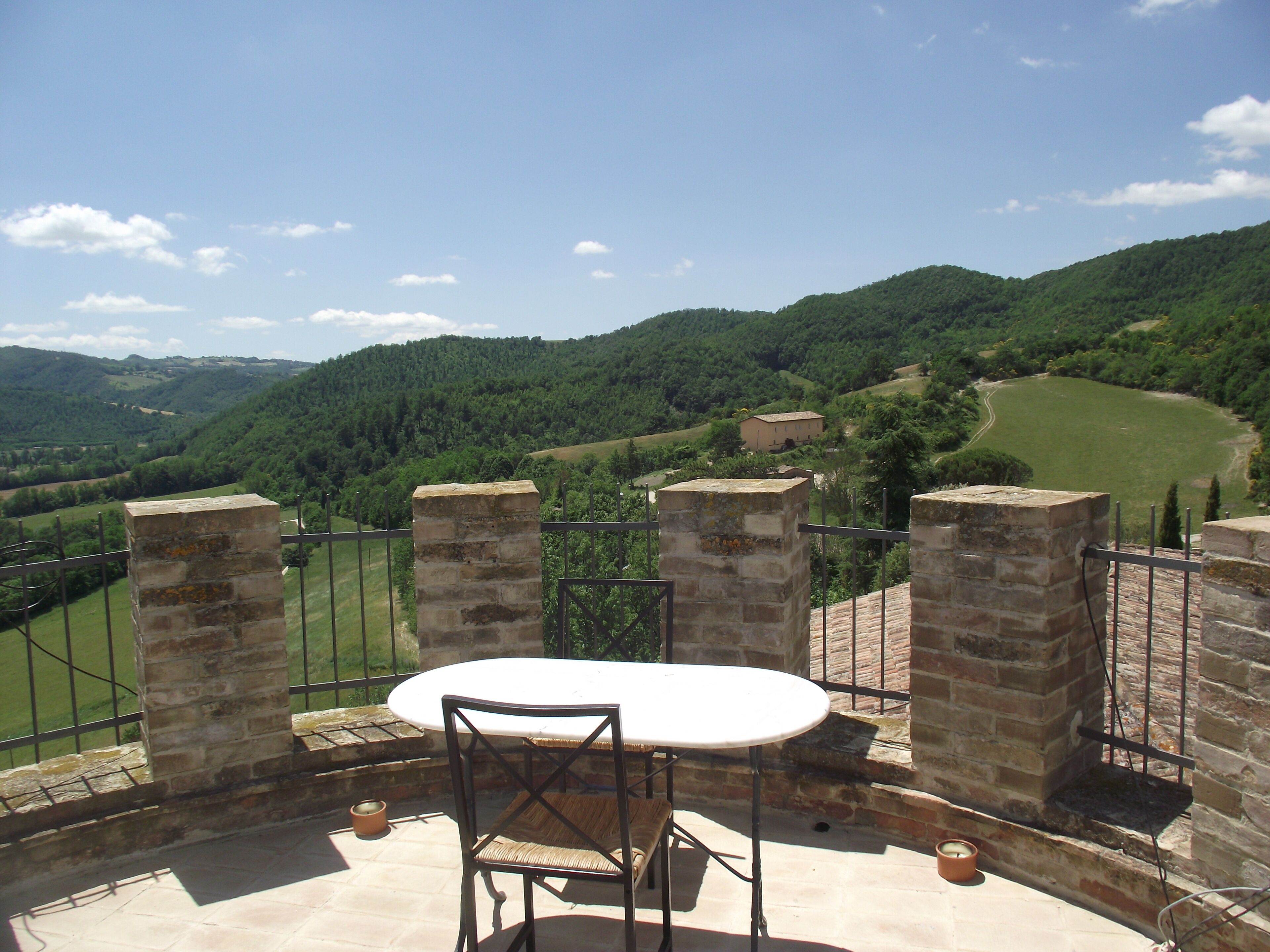Une terrasse avec une table et des chaises, offrant une vue sur une vallée verdoyante et des collines lointaines.