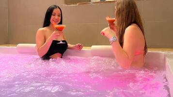 Deux femmes sont assises dans un jacuzzi éclairé de lumières roses et tiennent chacune un verre à martini.