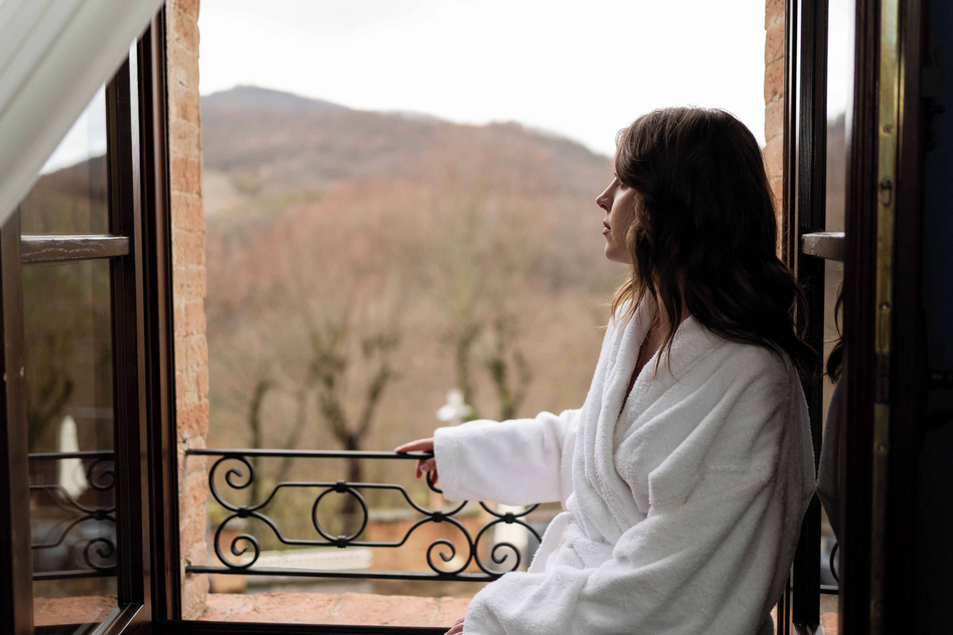 Una persona con bata blanca sentada junto a una ventana con vistas a un paisaje montañoso.
