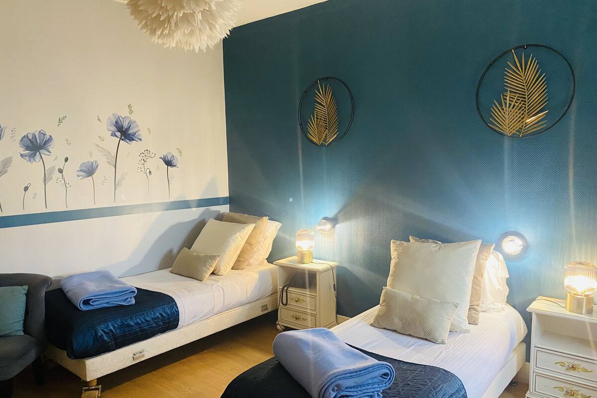 A hotel room with two beds, a nightstand with lamps, and a wall with floral artwork.