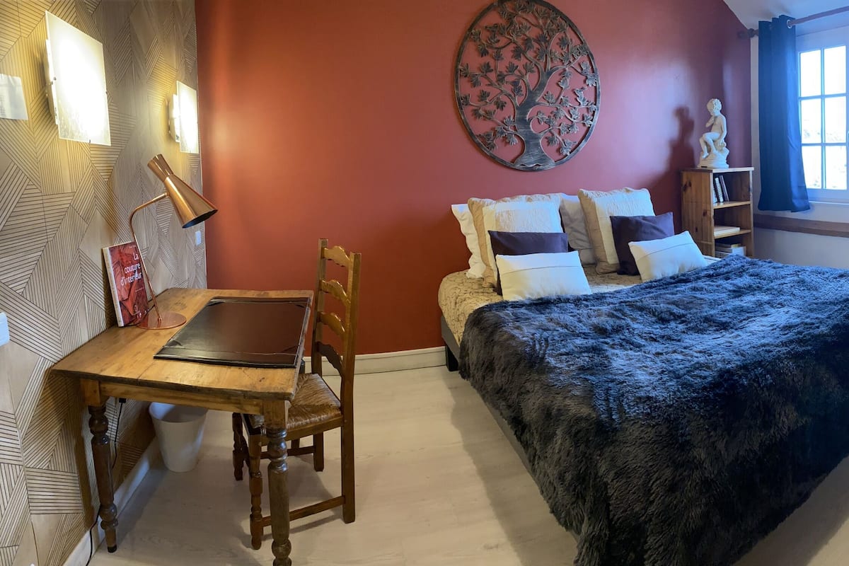 A cozy bedroom with a bed, a wooden desk, a chair, a bookshelf, and a radiator.