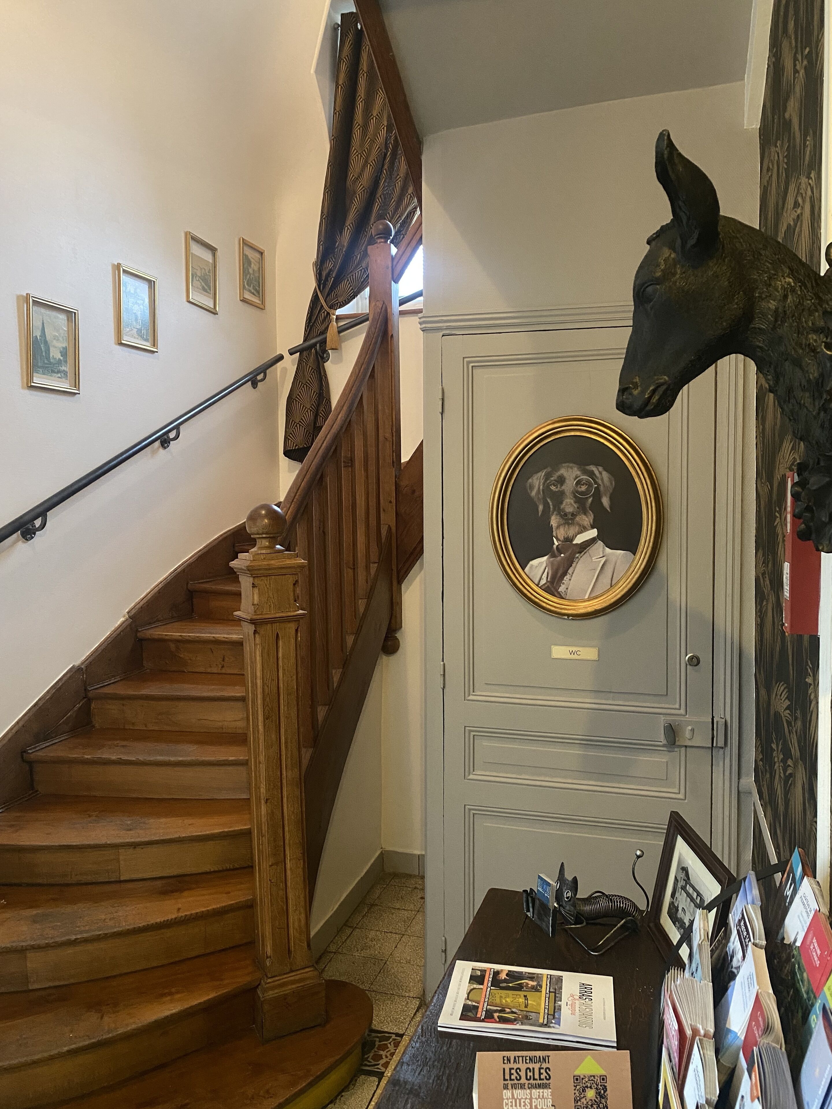 A staircase with wooden steps and a handrail, a door with a mounted dog portrait, and a wall with framed pictures.