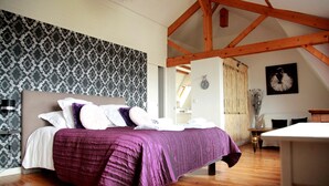 A bedroom with a large bed, wooden beams, a patterned wallpaper, and a clock on the wall. - Hôtel Belle Vue (Coucy-le-Chateau-Auffrique)