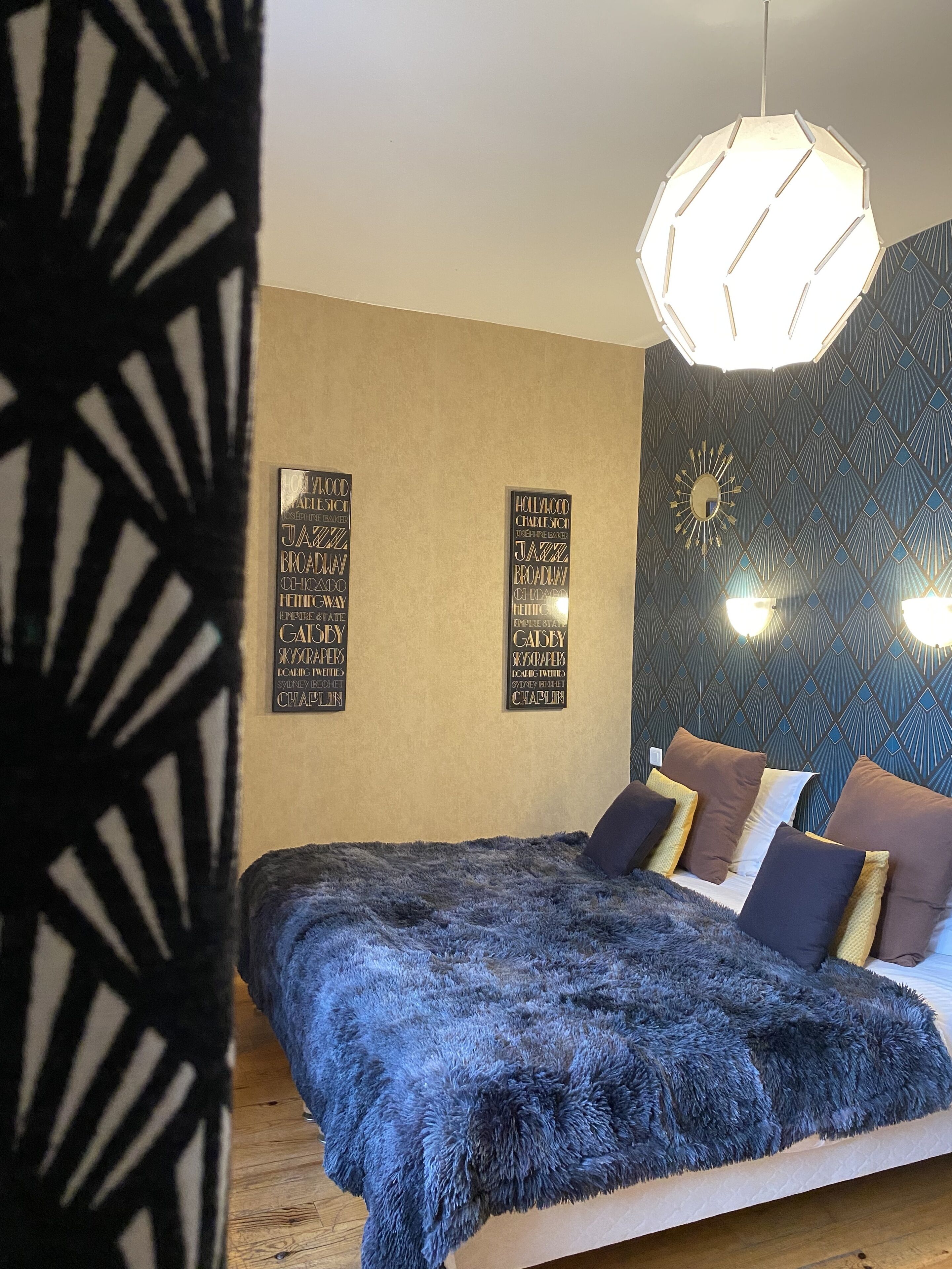 A bedroom with a large bed, a hanging light fixture, and two wall-mounted signs listing famous theaters.