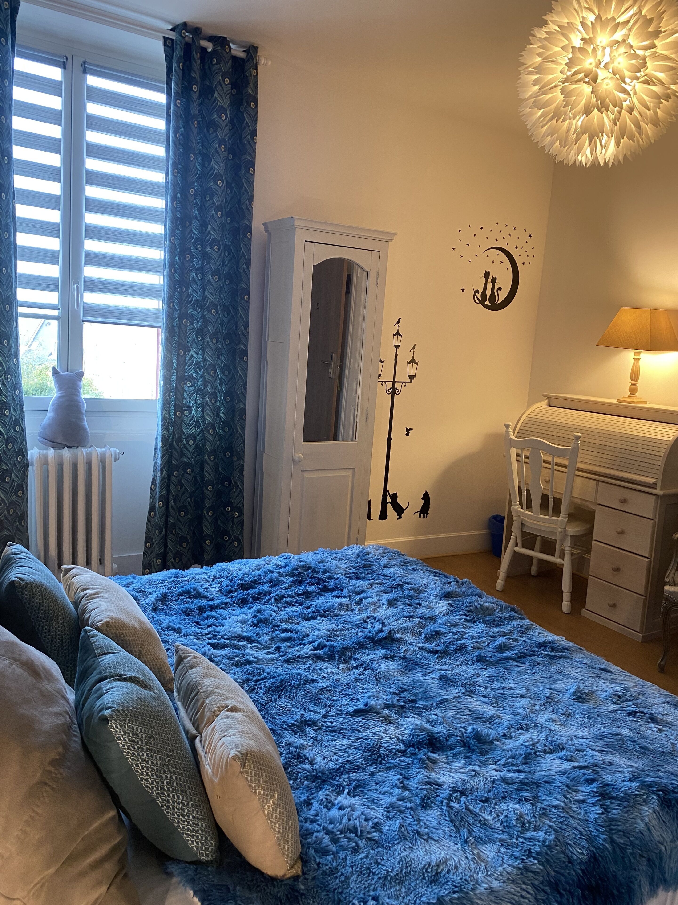 Une chambre à coucher avec un grand lit bleu, une commode blanche, un bureau et un radiateur.