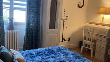Une chambre à coucher avec un grand lit bleu, une commode blanche, un bureau et un radiateur.