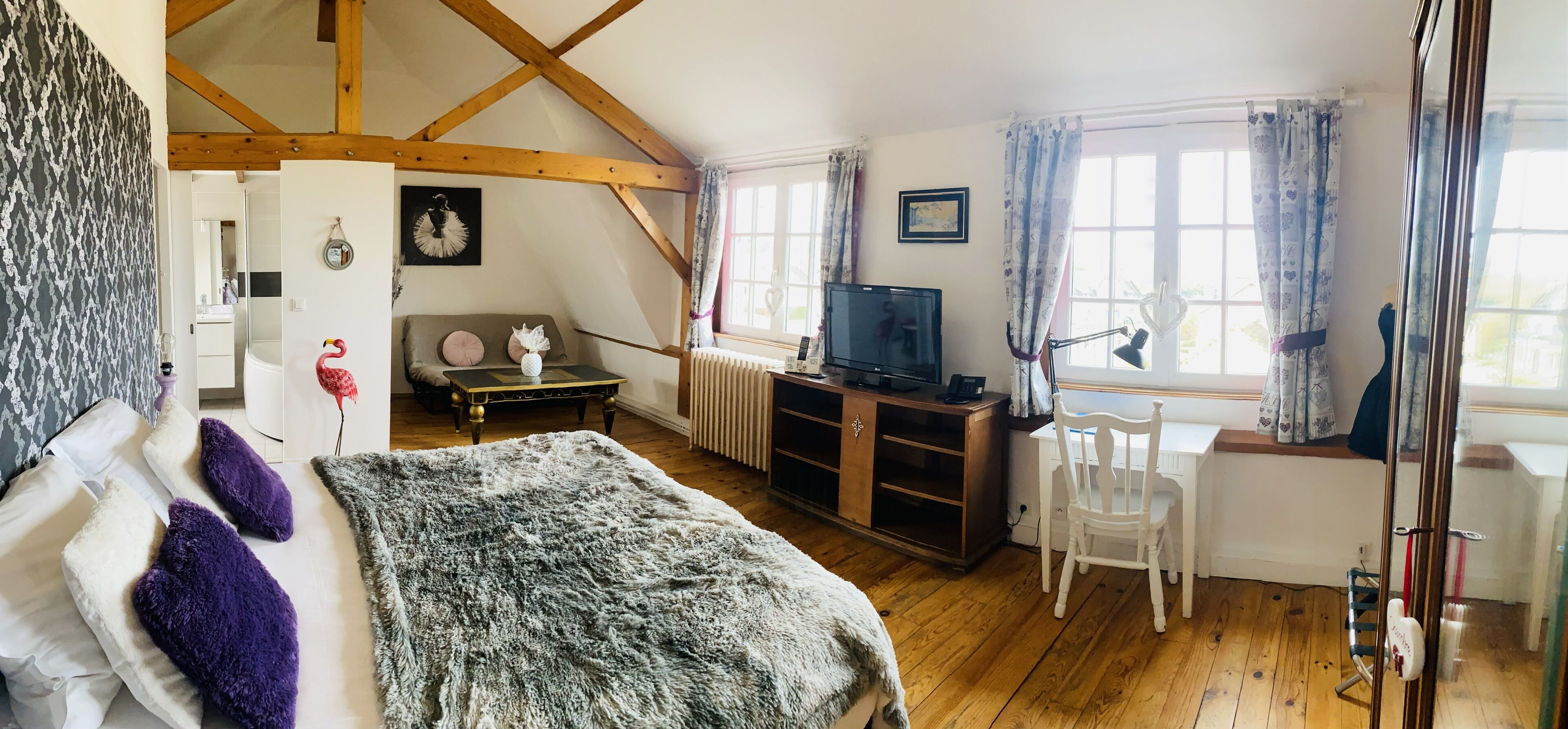A cozy bedroom with a bed, a desk, a chair, a TV, and a radiator.