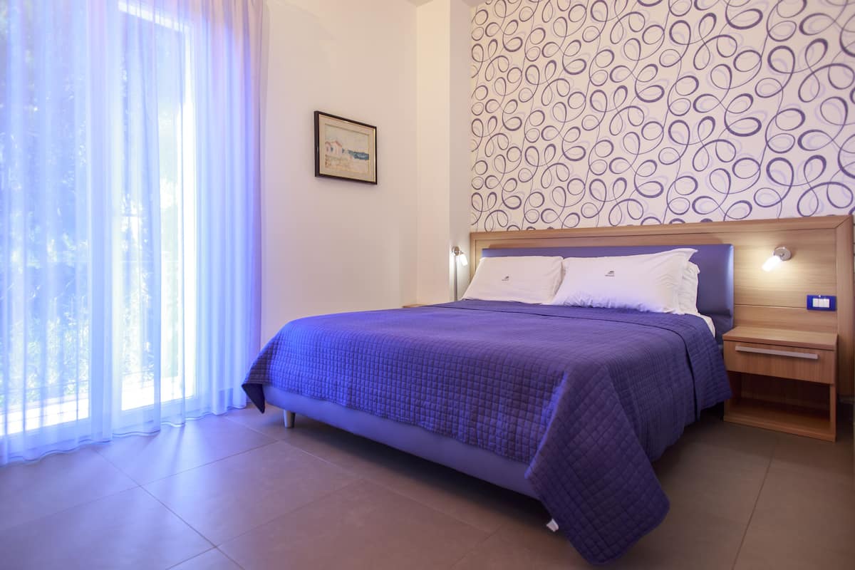 A bedroom with a bed, nightstands, a window with curtains, and a patterned wall.