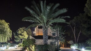 A nighttime view of a building with a palm tree in the foreground, surrounded by well-lit gardens and a paved pathway. - B&B Villaseta (Agrigento)