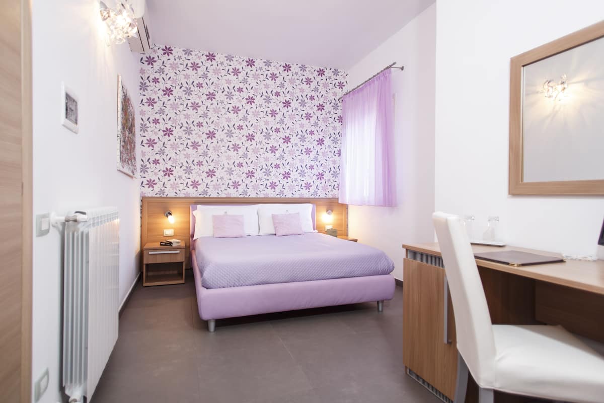 A bedroom with a bed, bedside table, lamp, and a desk with a chair.