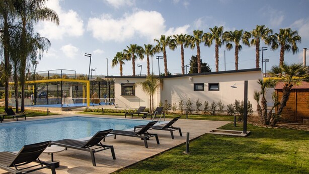 A swimming pool with lounge chairs, palm trees, and a modern building with a flat roof. - B&B Villaseta (Agrigento)