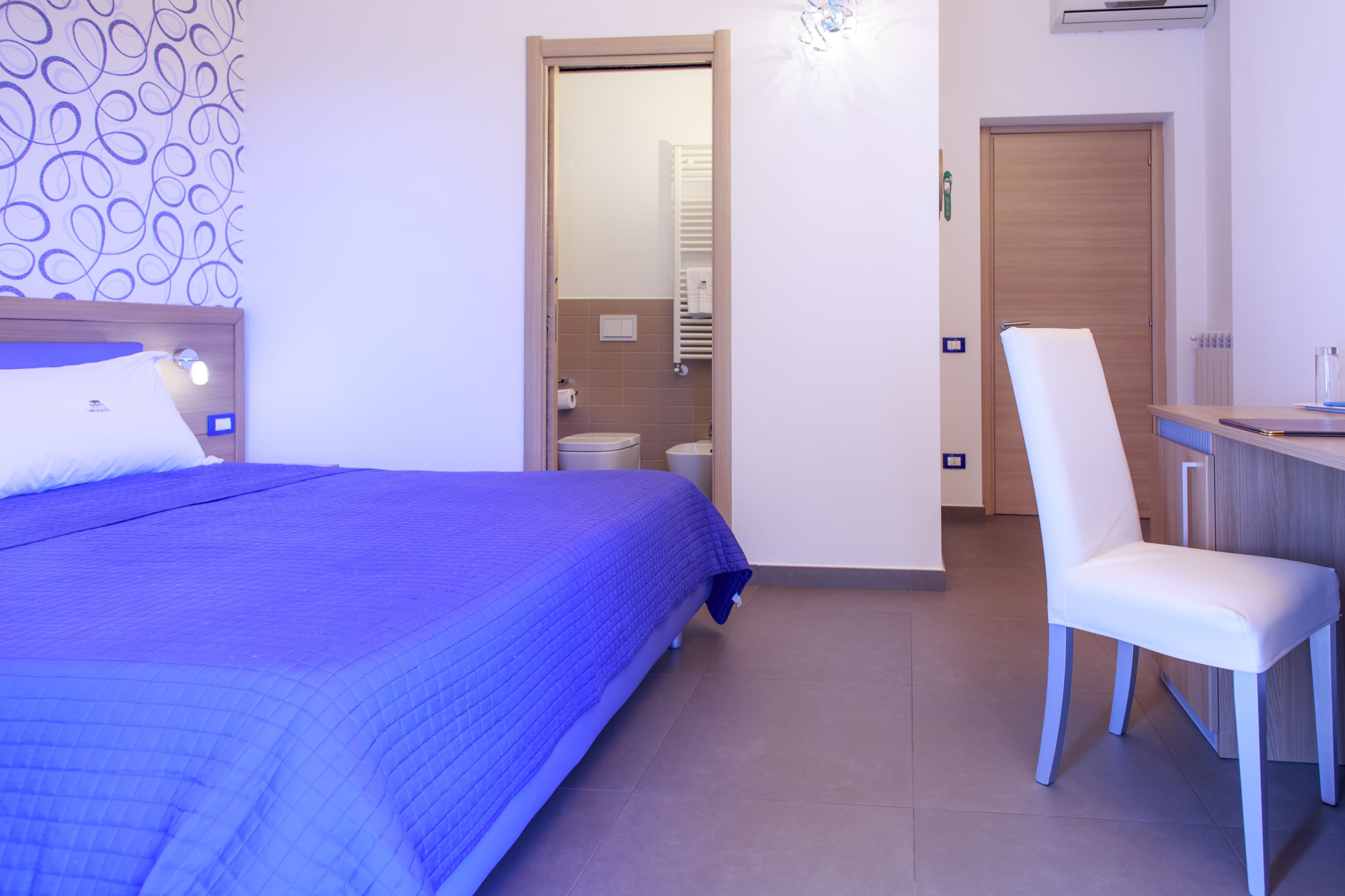 Une pièce comprenant un lit, une chaise, un bureau et une salle de bain visible à travers une porte ouverte.