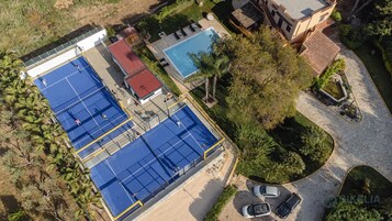 An aerial view of a property with multiple tennis courts, a swimming pool, and a landscaped garden.